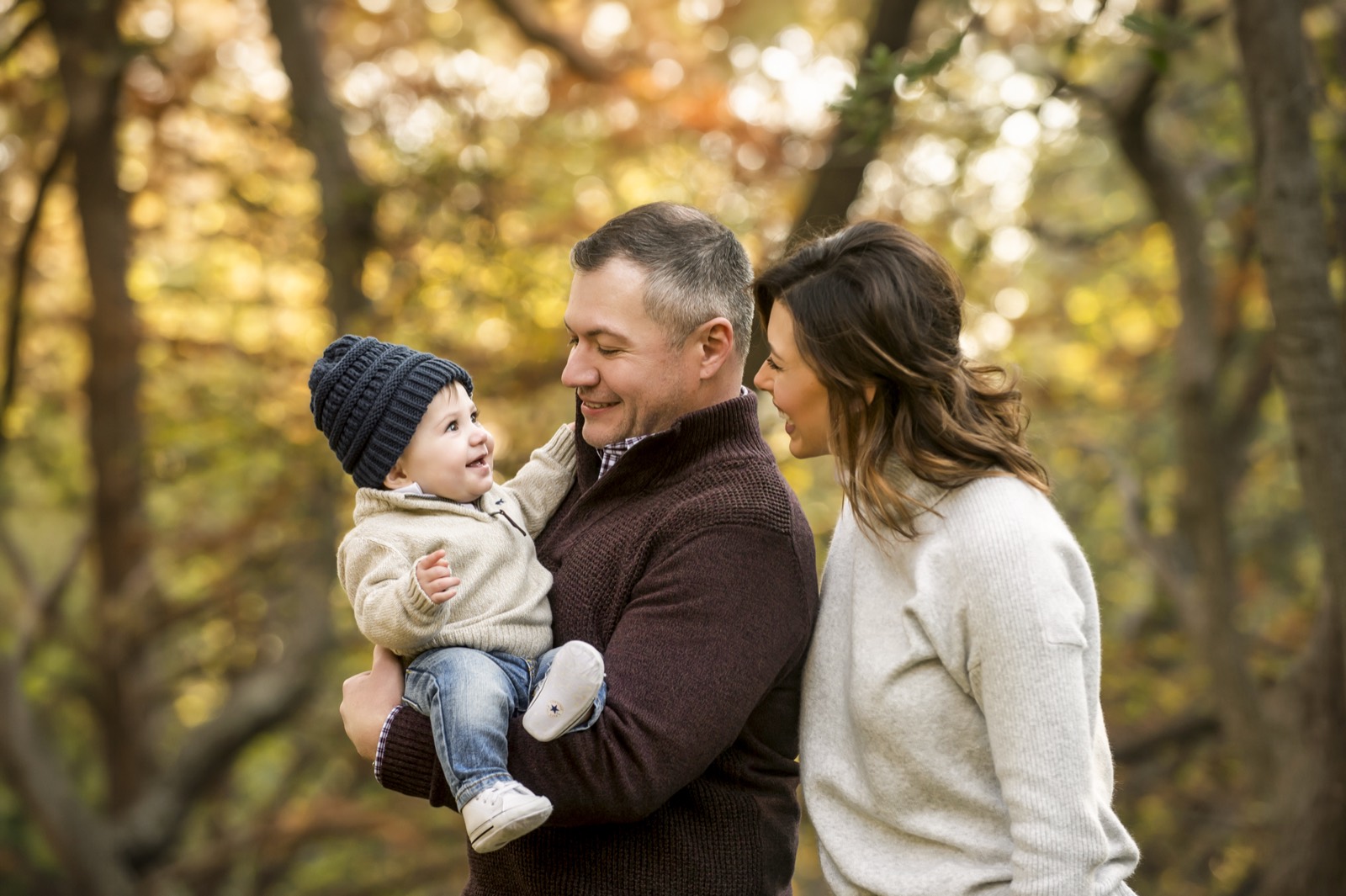 Dallas parents holding their baby in a beanie among warm autumn leaves during a fall family mini session